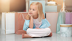 Child, fashion and shopping bags while looking bored and waiting in a kids clothing shop, store or boutique with cute girl sitting on floor. Little kid shopper or customer with sale purchase packages