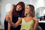 Woman holding mirror at salon looking at new hair with hairdresser for professional beauty treatment. Smile, stylist and happy customer with fresh hairstyle and natural makeup in chair at hair salon 