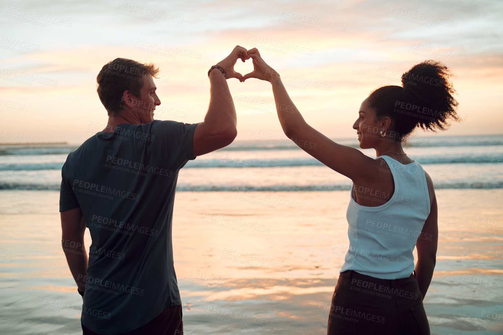 Buy stock photo Beach, couple and heart hand at sunset with happy people bonding together on Mexico holiday break. Care, love and trust in interracial romantic relationship with people enjoying ocean sky at dusk.