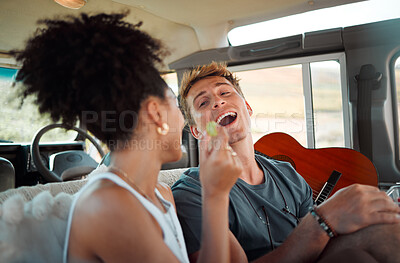 Buy stock photo Couple eating on road trip, people travel in car with friends and vacation in Canada together. Black woman giving grape to boyfriend, funny man with open mouth and interracial love in camper drive