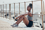 Beach, relax and woman runner thinking after an outdoor cardio workout in nature by ocean. Tired African athlete, running and fitness girl sitting on promenade to breathe, calm and rest after workout