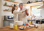 Love, breakfast and senior couple dance in kitchen for romance and happy life together in house. Married retirement people smile with happiness enjoying cooking dancing break in Canada home.

