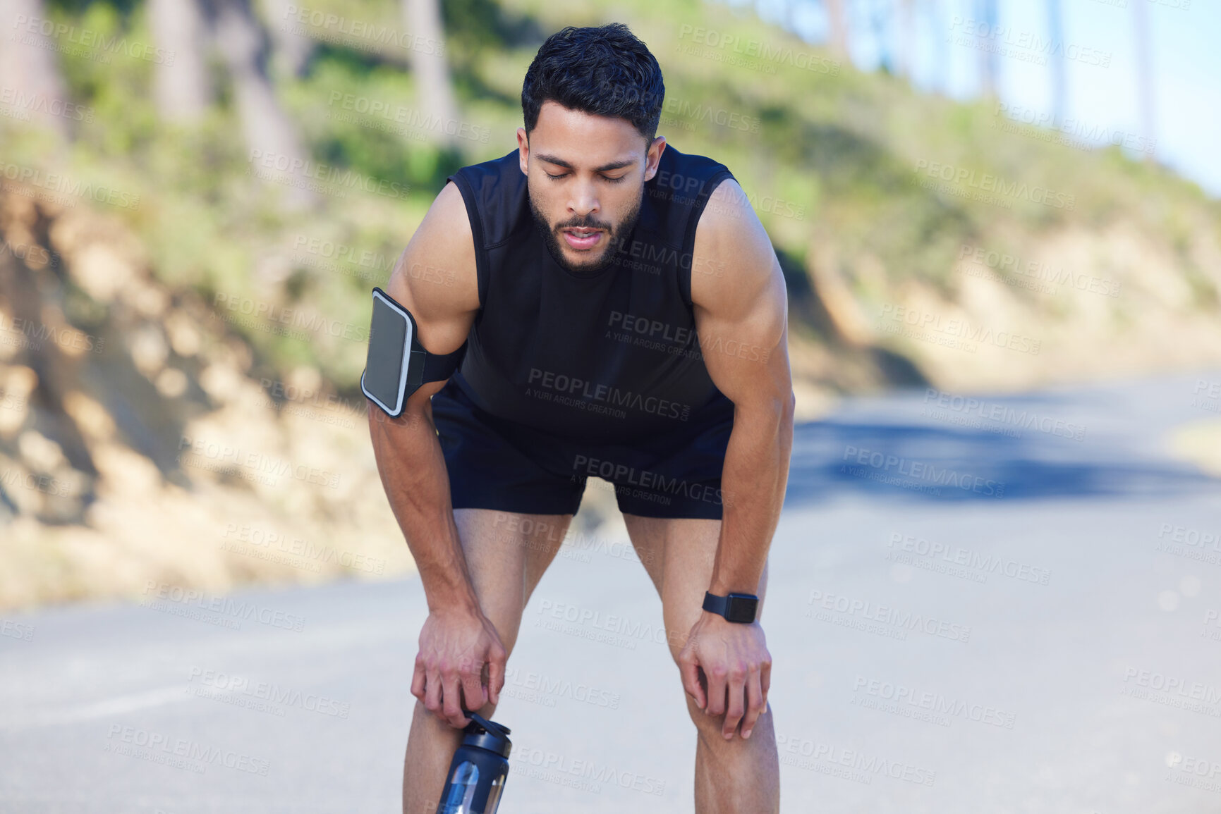 Buy stock photo Road, runner and tired man on a break after running exercise, cardio training and workout outdoors in nature. Sports, fitness and out of breath athlete with fatigue resting and holding a water bottle