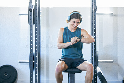 Fitness, man checking time and exercise for sports training monitoring workout while sitting on a bench at the gym. Athletic sport male looking at smartwatch while resting on gyming equipment indoors