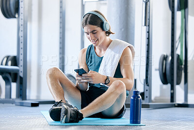 Buy stock photo Man check social media in gym, workout music playlist on smartphone and typing online conversation. Happy young athlete sitting on floor, sports health application and fitness lifestyle technology