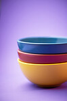 Color, container and group of ceramic bowl, kitchen equipment or plastic plate tower for soup, cereal or breakfast food. Colorful stack of blue, yellow and maroon objects on purple background studio