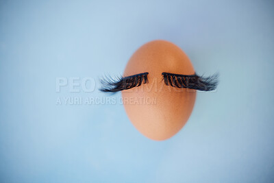 Buy stock photo Beauty, makeup and eyelashes with an egg on a blue background in studio with mockup. Cosmetics, mascara or abstract with an embryo and fake lashes with product placement for marketing or advertising