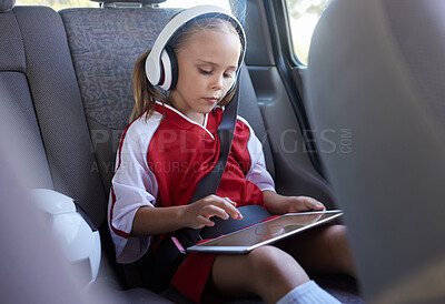 Buy stock photo Child with tablet, headphones and safety belt in the car going home after soccer match, game or practice. Young girl in sports gear playing educational games online on tech device after training