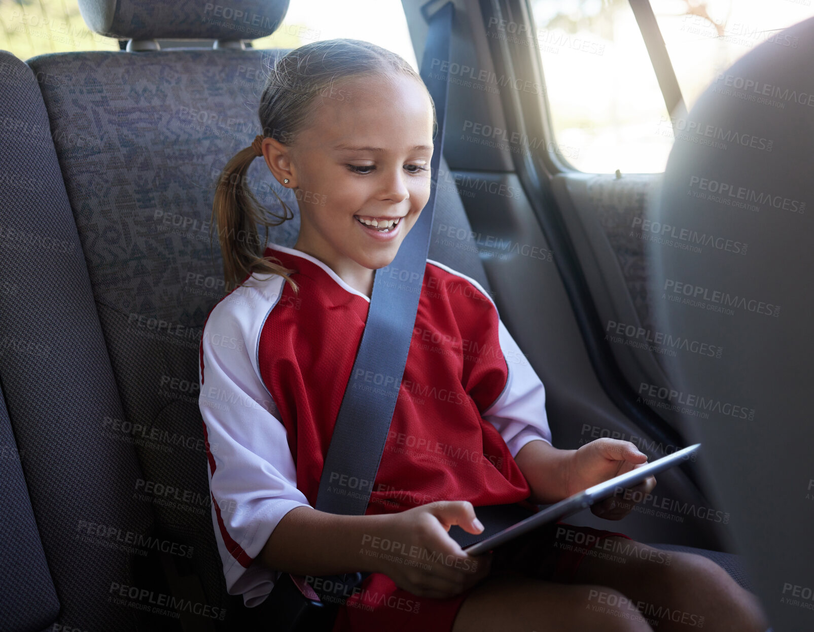 Buy stock photo Happy, girl child and with tablet in car smile, browse online and use social media apps while buckled up. Female kid, use digital device or after practice, share winning soccer match or playing game 