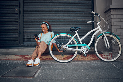 Bike, woman and headphone with phone in city relax, with bicycle and happy texting, social media apps and chat. Girl, lady and with eco friendly transportation, trendy or edgy look sit on sidewalk