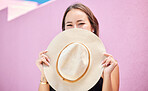 Travel, fashion and summer hat with a woman tourist in the city on a pastel color pink wall background. Happy, holiday and tourist with a female traveler covering her face with a sunhat in town