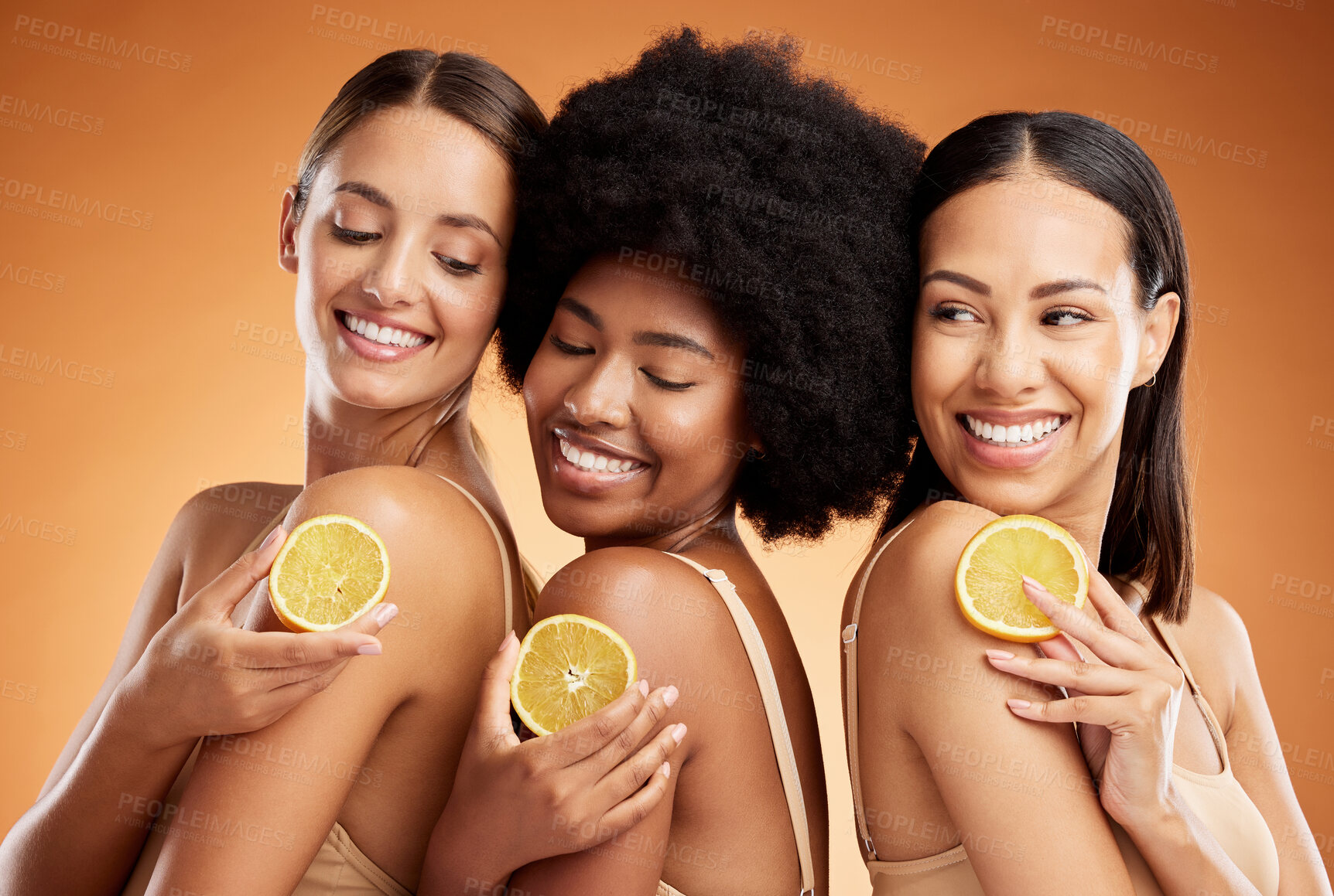 Buy stock photo Skincare, diversity and women, beauty and lemon for health, wellness and nutrition on orange studio background. Friends, smile and happy models with fruit for vitamin c, healthy or glowing skin.
