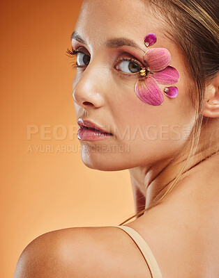 Buy stock photo Model, flower and eye with fashion in portrait with smile for makeup, cosmetics or beauty against backdrop. Woman, orchid and floral art for eyes with skincare, happy and face orange background