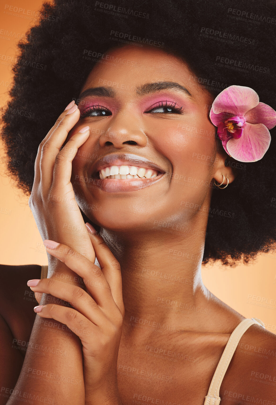 Buy stock photo Flower, model and makeup with afro in closeup for fashion, cosmetic or beauty with orange backdrop. Woman, pink orchid and hair for cosmetics with smile, happy and glow on skin with studio background