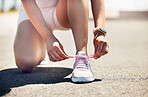 Fitness, exercise and shoes with a sports woman tying her laces while running on an asphalt road or street. Workout, training and cardio with a female athlete getting ready for a run routine