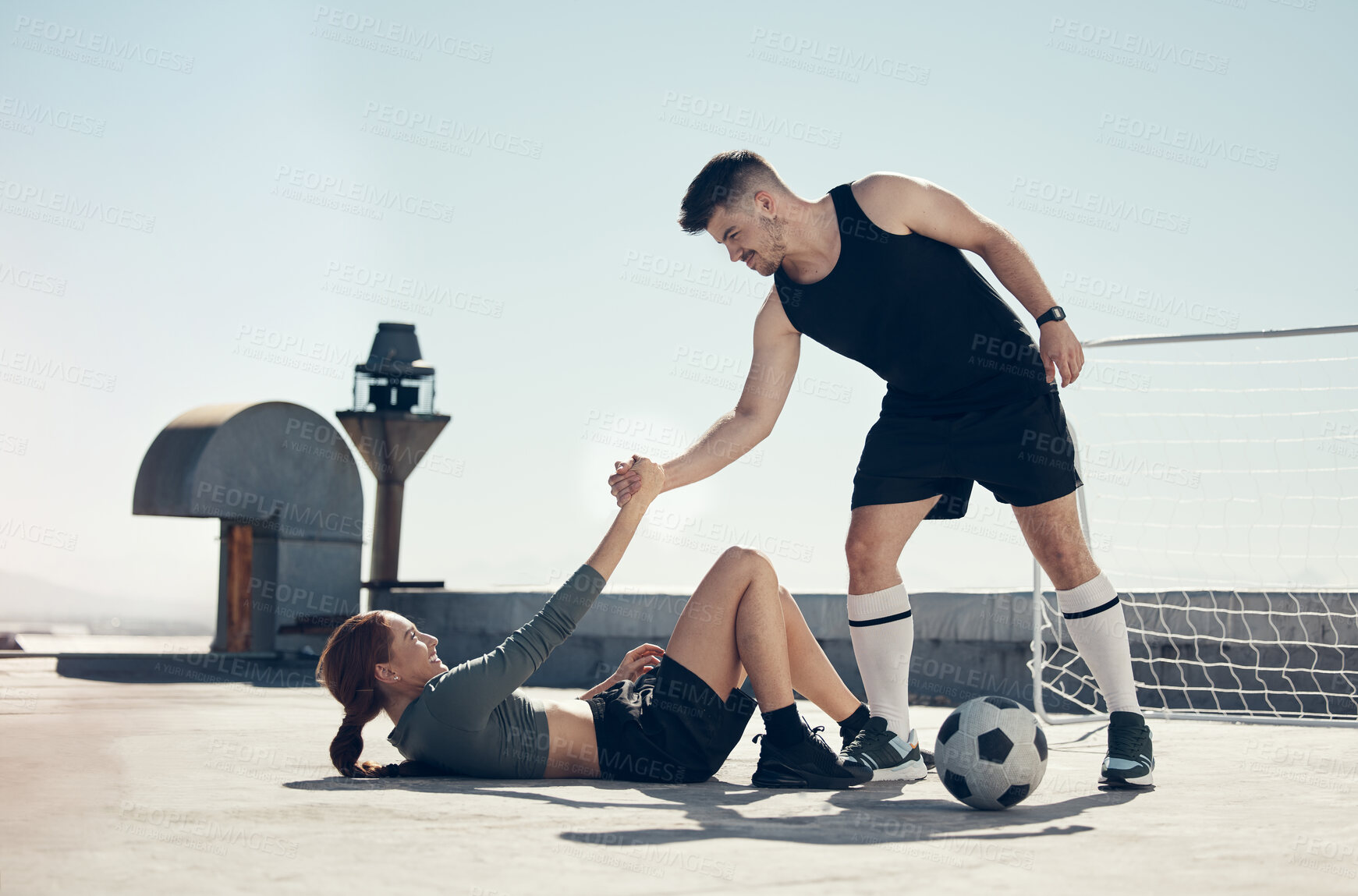 Buy stock photo Teamwork, soccer and helping player in sports game, playing football on urban rooftop. Helping hands, inspiration and man giving support to injured woman doing fitness, exercise and training in city