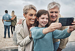Phone, selfie and grandparents with a child at the beach while on family adventure, journey or holiday. Happy, smile and senior couple in retirement taking picture with girl while on seaside vacation