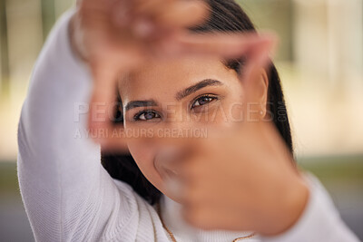 Buy stock photo Hands, frame and eyes with a woman looking through her fingers while framing her face outdoor. Portrait, girl and happy with a young female posing behind a hand sign on a blurry background outside