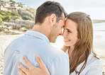 Couple, love and hug on a beach together for an engagement announcement or anniversary by the sea. Young man and woman smile feeling happy and romantic by the ocean water and sand with happiness