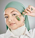 Muslim arab woman beauty, jade roller and facial skincare, cosmetics product and aesthetic wellness on studio background. Portrait islamic hijab, model face and green stone massage, self care or glow