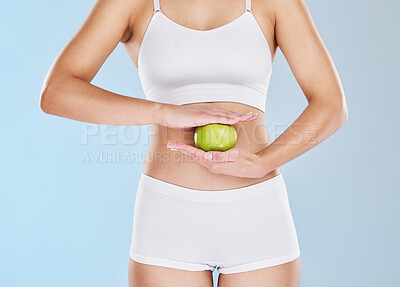 Buy stock photo Health, weight loss and apple on stomach of woman in underwear for nutrition, diet and vegan lifestyle. Wellness, fitness and digestion with hands of girl and fruit on slim body with blue background