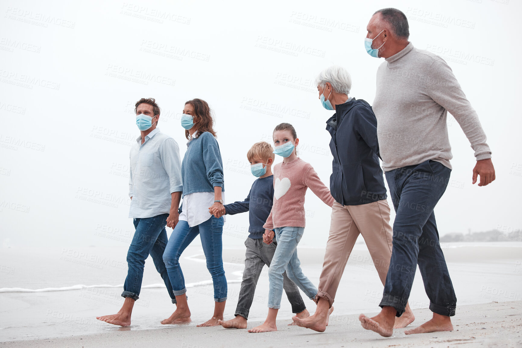Buy stock photo Covid, mask and big family walking together on a beach with mother, father and children outdoor. Parents, kids and grandparents walking on sand at the ocean water waves holding hands with love