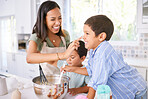 Family baking and mother teaching children to bake cake in the kitchen of their home. Happy latino kids and woman play, cooking and laugh together while learning about food and being playful in home