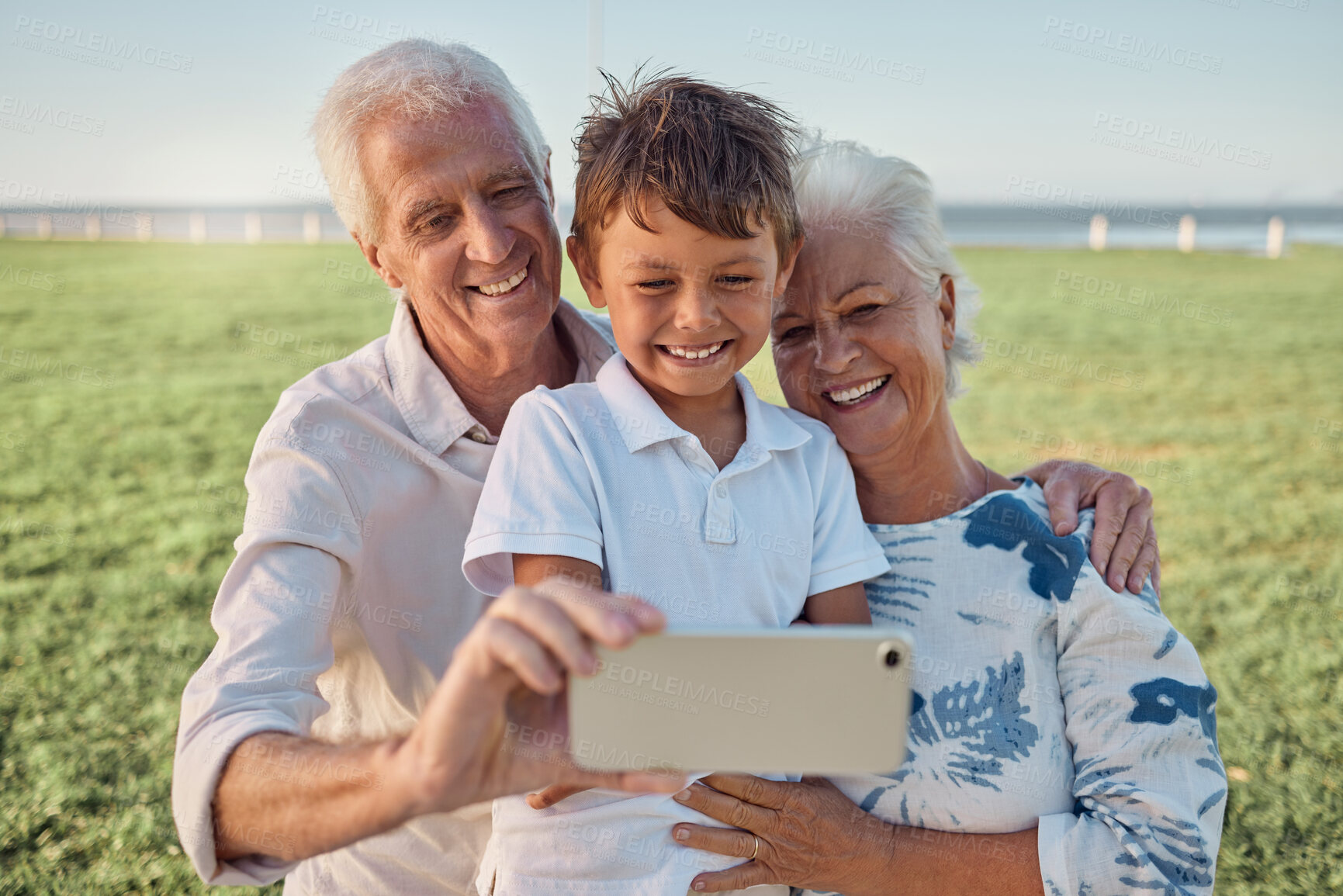 Buy stock photo Kid, grandparents and phone selfie on grass in park spending time together on the weekend. Grandma, grandpa and boy child with smile on face, happy family take outdoor portrait on smartphone on field