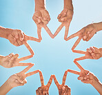 Teamwork, community and group support with fingers in a star shape from below against a blue sky background. A diverse crowd of people with hands joined together for motivation, unity and peace 