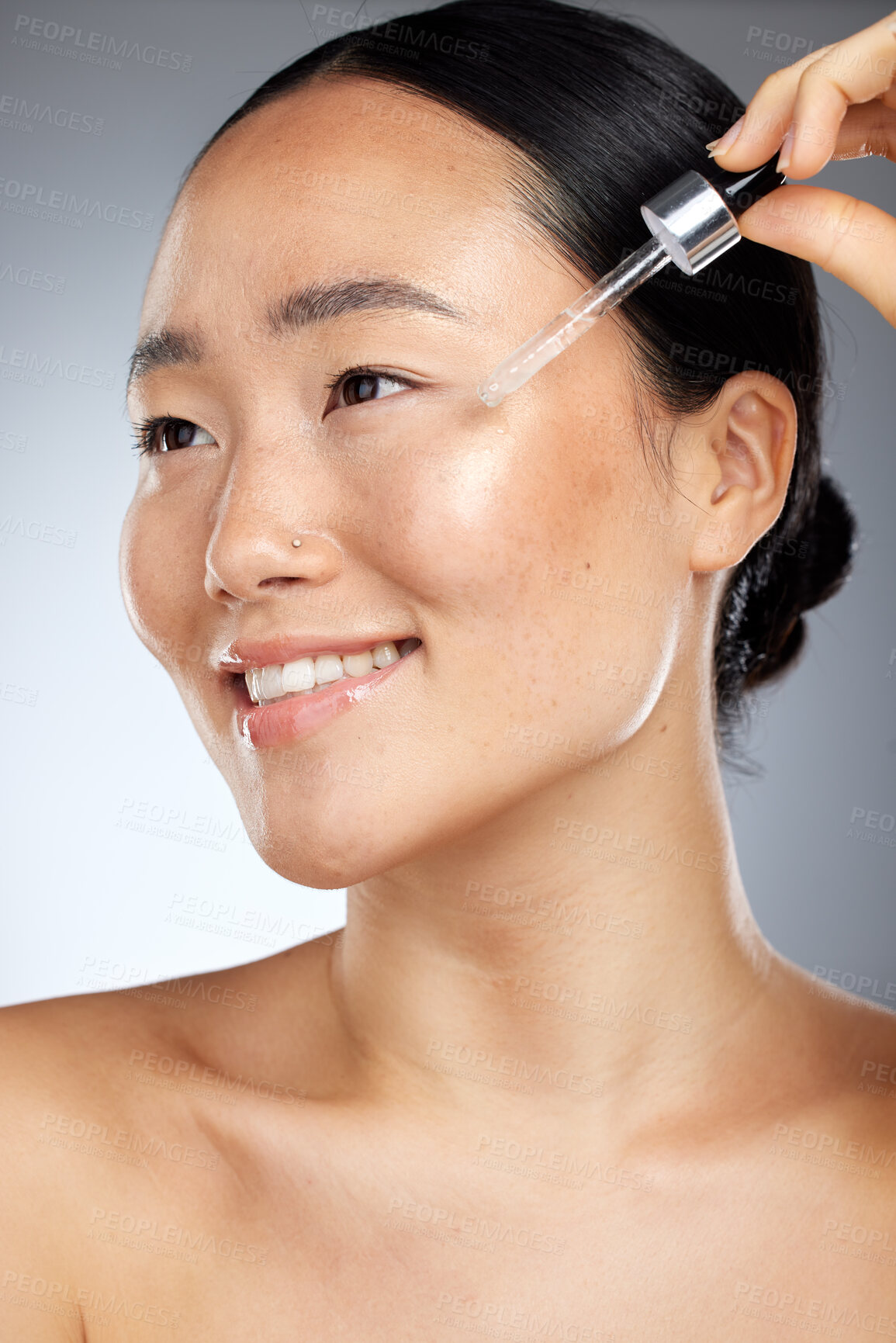 Buy stock photo Skincare, face oil and woman with wellness for her skin against a grey studio background. Happy, smile and young Asian model with a facial serum for body healthy, dermatology and a beauty glow