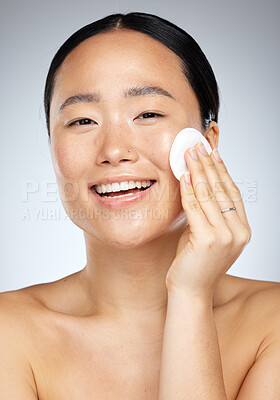 Buy stock photo Skincare, beauty and woman with cotton pad for facial cleaning against a grey studio background. Happy, smile and portrait of a young Asian model with cotton for face wellness, clean body and makeup
