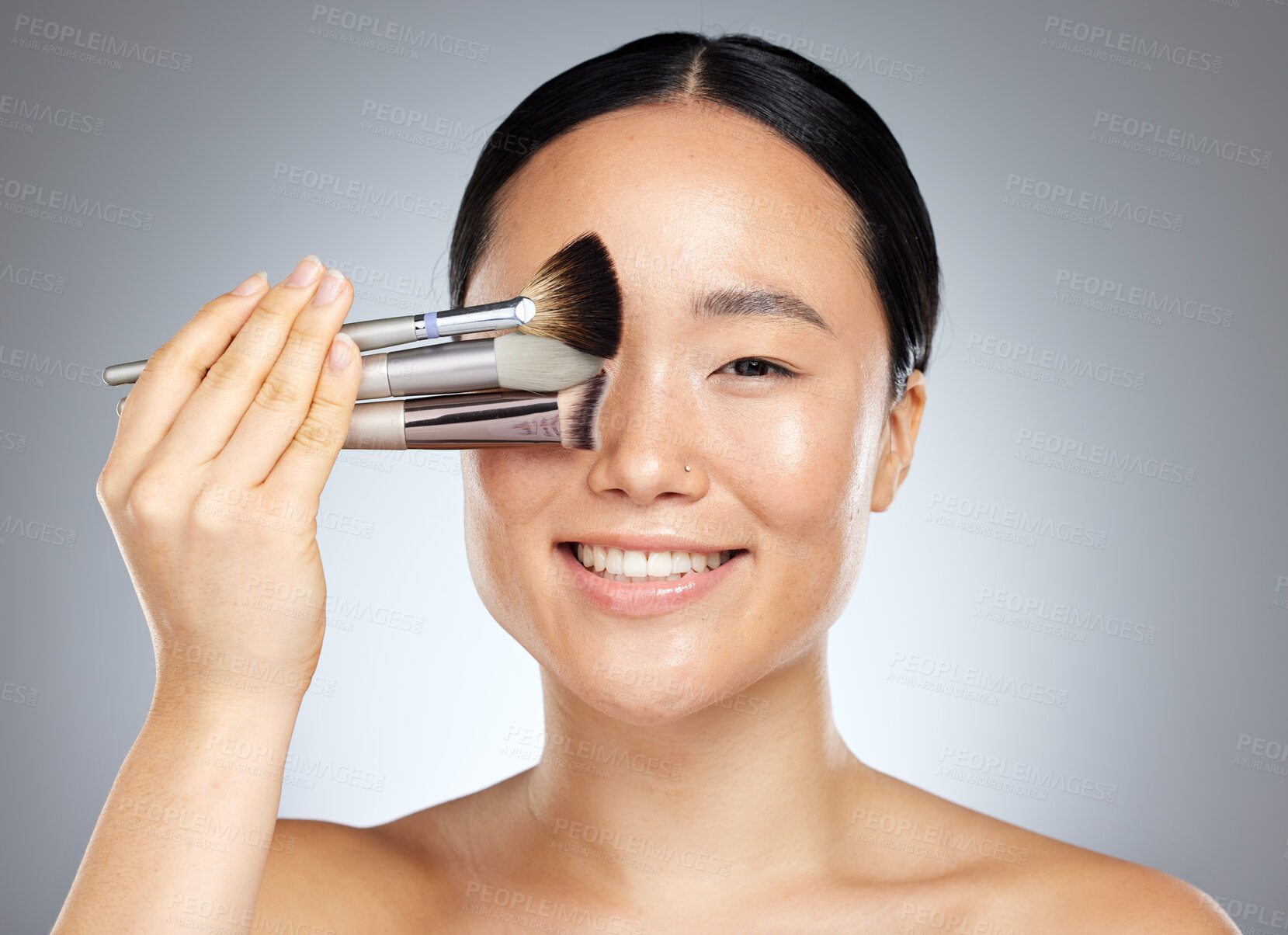 Buy stock photo Beauty, makeup and woman with brush for cosmetics against a grey mockup studio background. Portrait of a young, happy and Asian model with a product for facial cosmetic care and mock up space