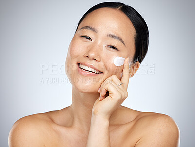 Buy stock photo Face, skincare and beauty with a model asian woman applying lotion or moisturizer to her skin in studio. Cosmetics, antiaging and wellness with a young female inside to promote a skin product