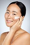 Face, beauty and skincare with an model asian woman in studio on a gray background for wellness. Luxury, health and cosmetics with a young female using an antiaging product or lotion treatment