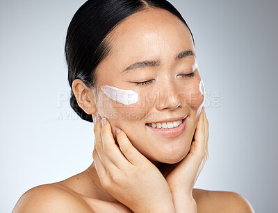 Buy stock photo Skincare, beauty and woman with smile using dermatology face cream or cosmetics against studio background. Face of happy, healthy and Asian model doing facial care for wellness and health of skin