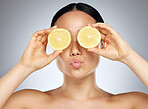 Woman, eyes and skincare holding fruit for healthy, nutrition or cosmetic treatment against a grey studio background. Hands of female in beauty care for skin facial with sliced lemons for vitamin C