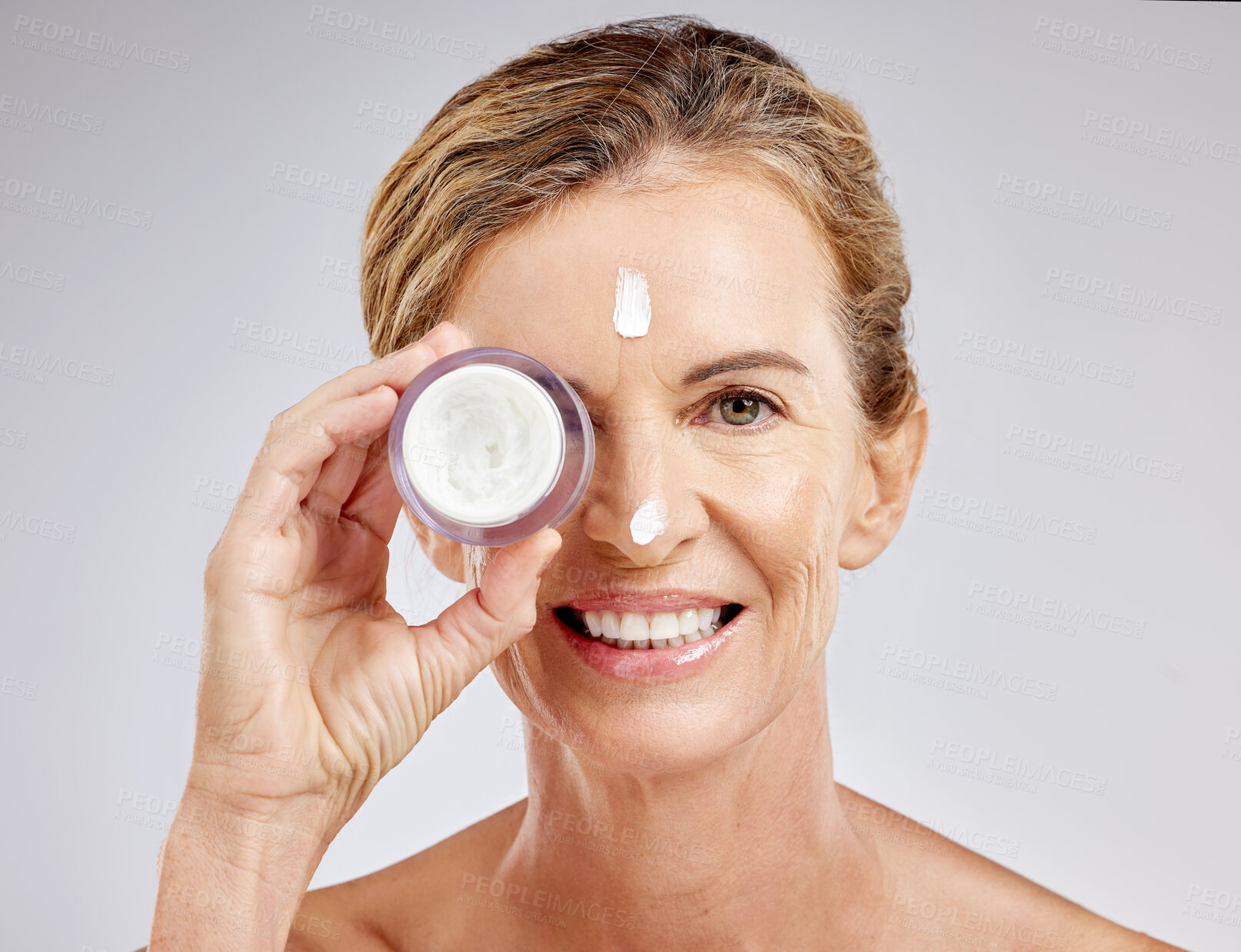 Buy stock photo Skincare, beauty and cream on face of mature woman with a smile for luxury spa self care on gray studio background. Senior, cosmetic wellness and nature cosmetic health with collagen lotion treatment