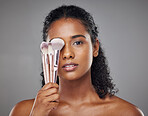 Beauty, black woman and portrait with brush cover on face for cosmetic powder or foundation tools. Makeup, cosmetics and brushes for beautiful girl model with grey studio mockup for marketing.

