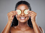 Skincare, portrait and woman with lemon on her eyes for health, beauty and wellness standing in a studio. Happy, smile and face of girl model from Brazil with citrus fruit isolated by gray background