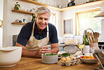 Senior, man and smile for cooking in portrait in kitchen while happy, proud or home. Elderly, chef or food in retirement for recipe, vegetables or ingredients on table, counter or house for happiness