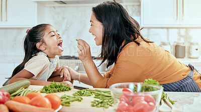 Buy stock photo Health, eating and food with mother cooking in kitchen with nutrition, vegetables and care. Home, lunch and healthy diet of asian family with young daughter tasting green veggies with mom.

