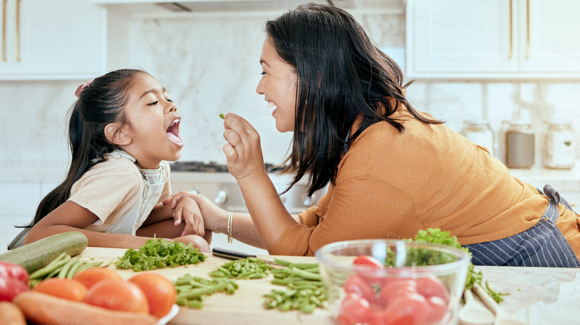 Buy stock photo Health, eating and food with mother cooking in kitchen with nutrition, vegetables and care. Home, lunch and healthy diet of asian family with young daughter tasting green veggies with mom.

