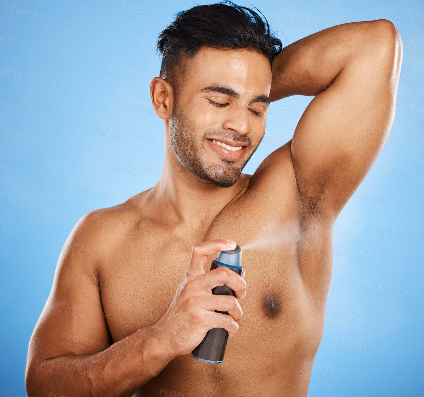 Buy stock photo Deodorant, beauty and grooming with a man model using antiperspirant in studio on a blue background. Body spray, aerosol and smell with a handsome young male spraying a scent product to his underarm