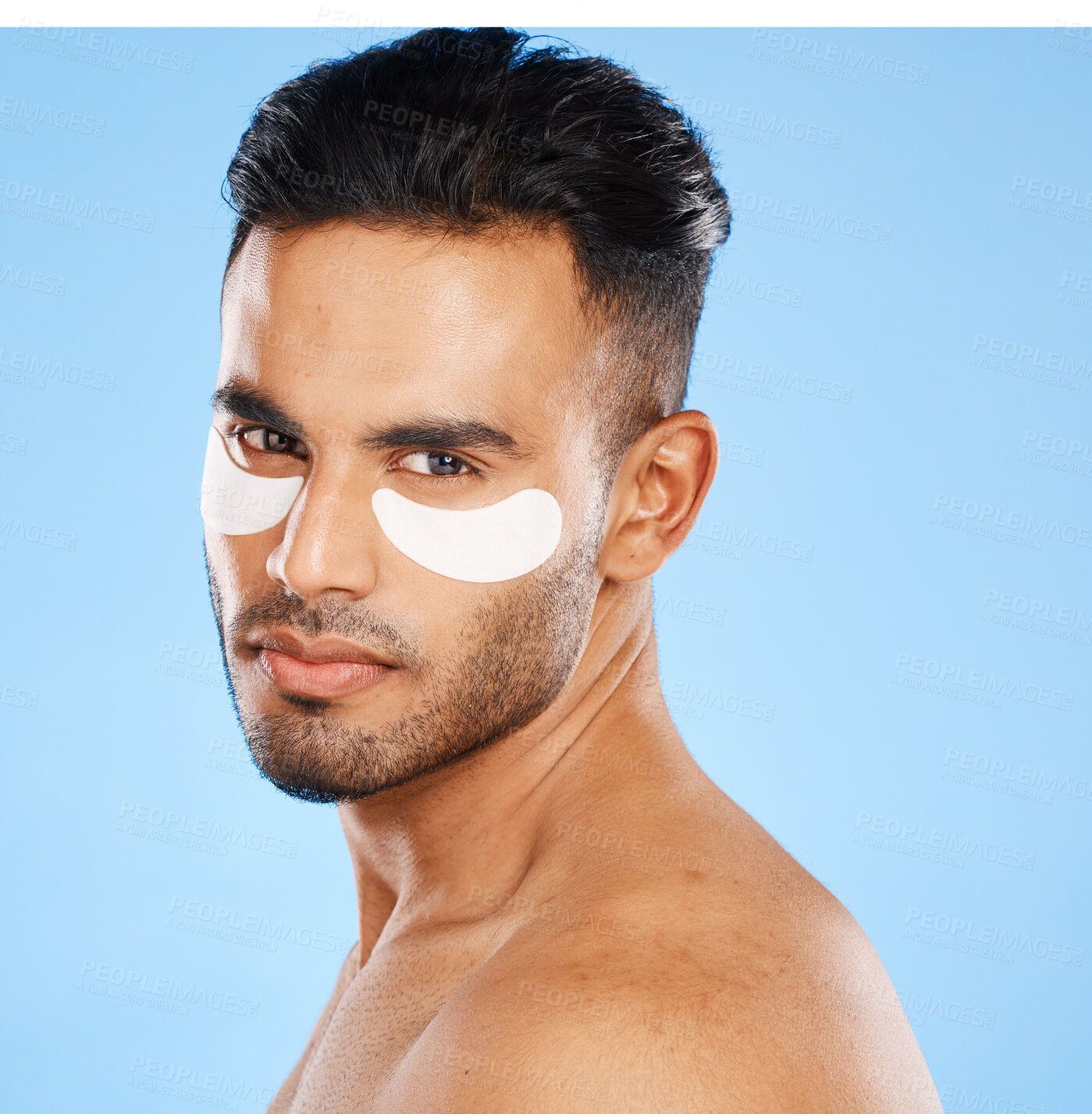 Buy stock photo Eye patches, skincare and portrait of man standing in studio doing a cosmetic beauty routine. Self care, healthy and male model doing face treatment with a facial product isolated by blue background.