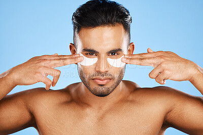 Man, eye patches and beauty for skincare, cosmetics or facial products against a blue studio background. Portrait of isolated male model in care for eyes applying patch for healthy skin or treatment