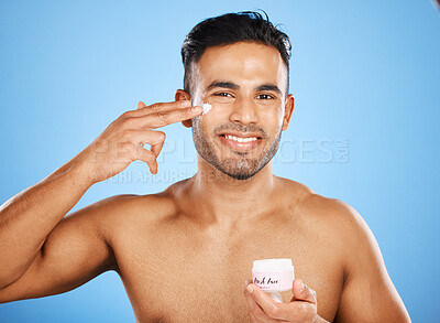 Buy stock photo Beauty, skincare and man with cream on face for healthy skin on blue studio background. Moisturizer, lotion and young model from Canada hydrate with creme for body care, beautiful or glowing skin.
