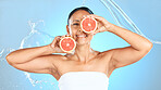 Beauty, cleaning and grapefruit by woman in studio for health, wellness and cosmetic treatment against blue background. Fruit, skin and model relax with detox, diet and water skincare splash product