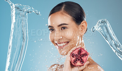 Buy stock photo Woman, beauty and water splash with pomegranate, skincare and happy against a blue studio background. Model, smile and shower with fruit for fresh, clean and healthy skin, face or hair with happiness