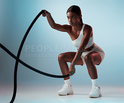 Buy stock photo Fitness, woman and rope exercise, sports training and workout for muscle, energy and wellness on blue background. Focus indian girl athlete moving battle ropes with speed, action and power in studio 