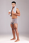 Portrait, water bottle and man with towel isolated on gray studio background. Fitness, wellness and healthy athletic male from India ready for hydration after training, exercise or workout mock up.
